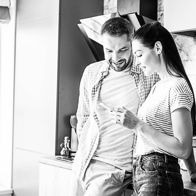 A couple standing in a kitchen looking at a phone